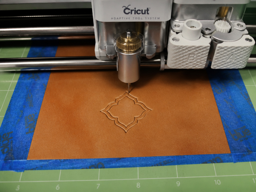 Close-up of a Cricut Maker knife blade cutting a precise shape into leather on a mat.
